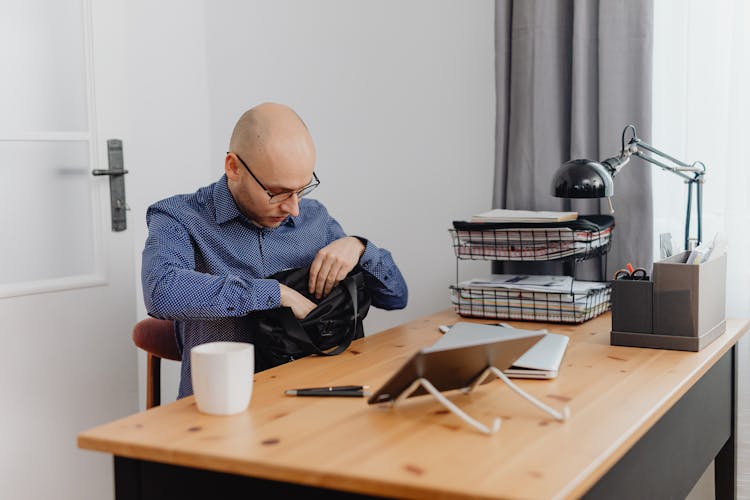 A Man Sitting By The Table Looking Inside A Black Bag