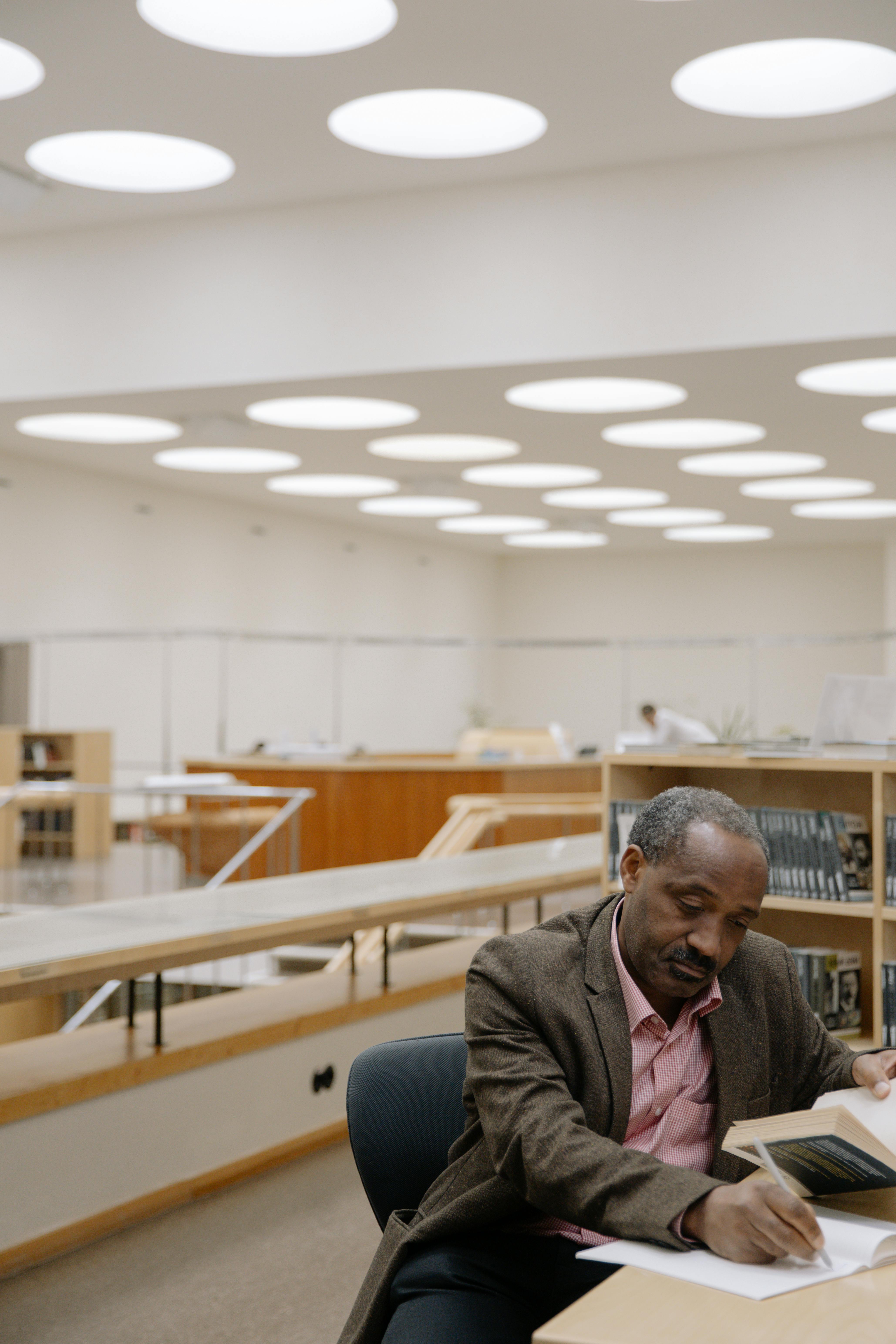 man holding a book and writing inside a library