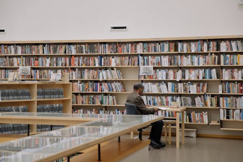 Man in Black Suit Jacket Reading Inside a Library
