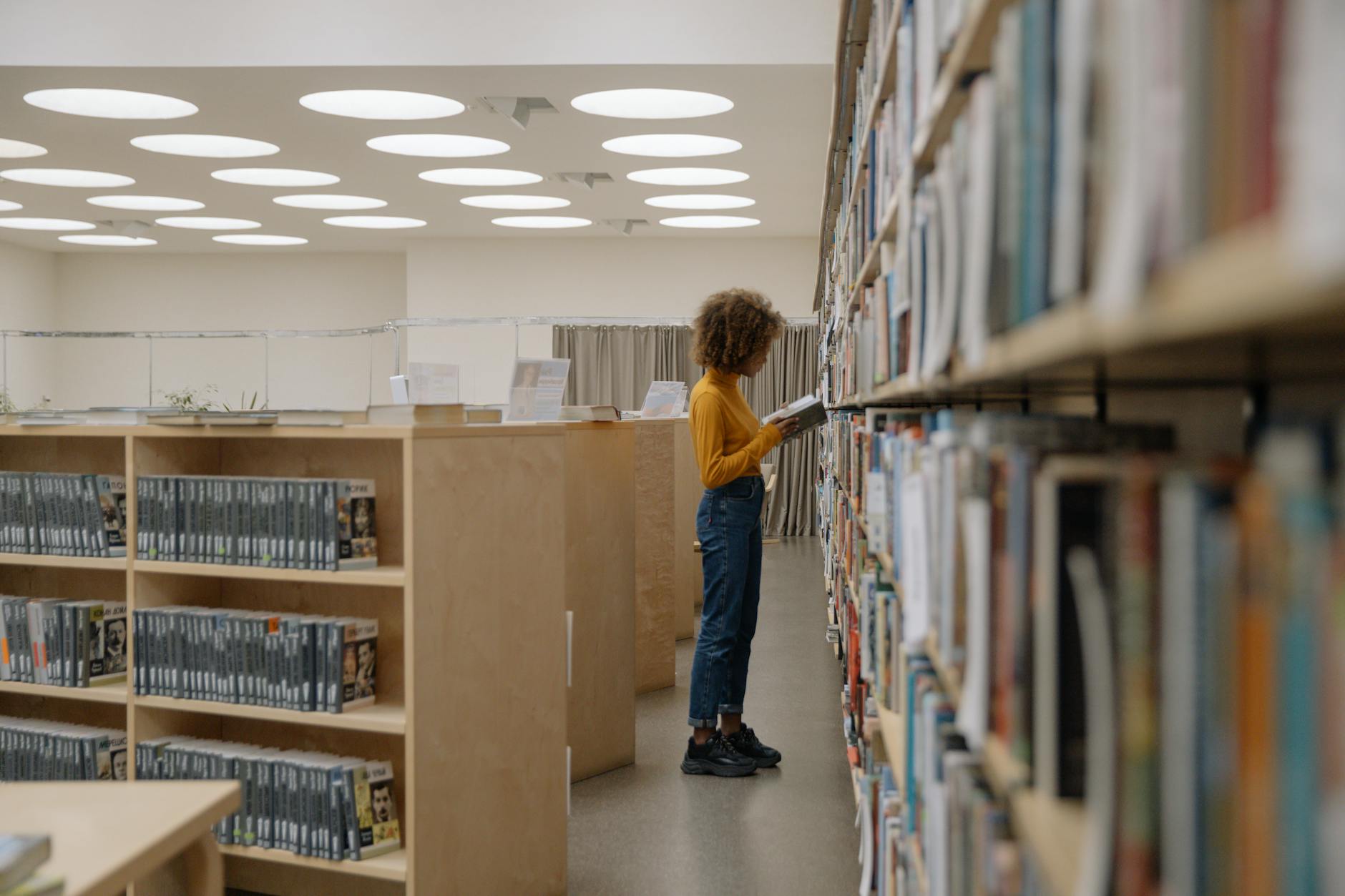Side view of a woman reading a book in a large, modern library with circular ceiling lights.