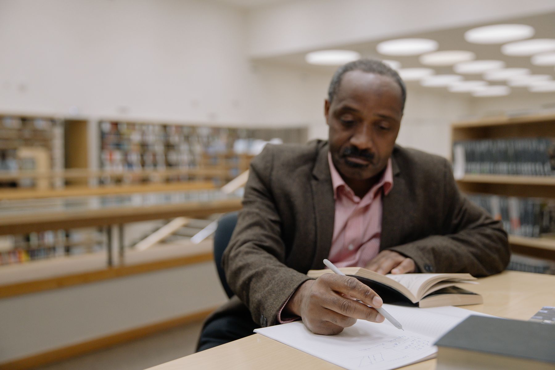A man reading and taking notes at a library table