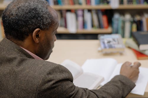 Free Man in Brown Suit Jacket Reading and Writing Inside a Library Stock Photo