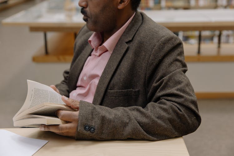 A Man In Suit Jacket Sitting At The Table Holding A Book