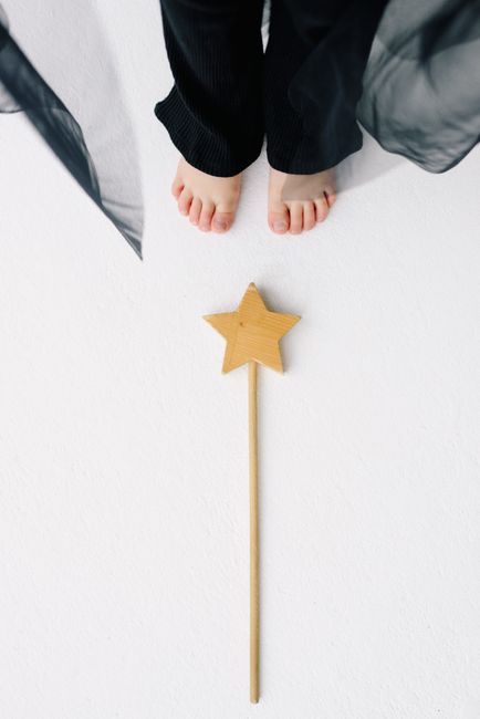 High angle shot of child's bare feet next to a wooden star wand on a white background.