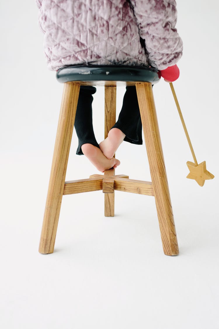 Back View Of A Child With Bare Feet And A Magic Wand Sitting On A Stool