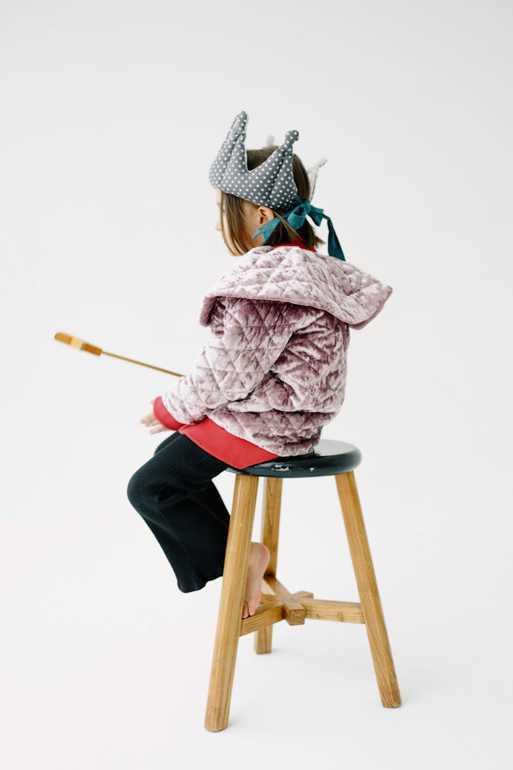 A Girl Wearing A Fabric Crown Sitting On A Wooden Chair