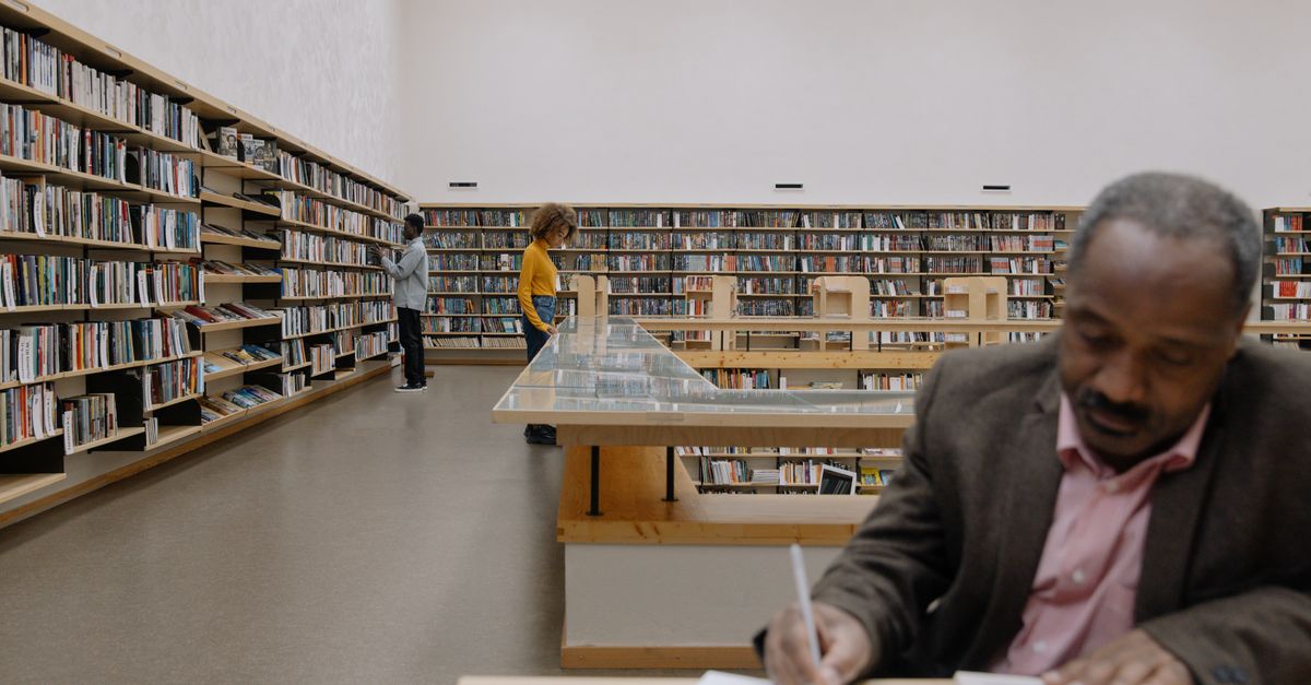 A diverse group of adults reading and studying in a spacious, modern library.