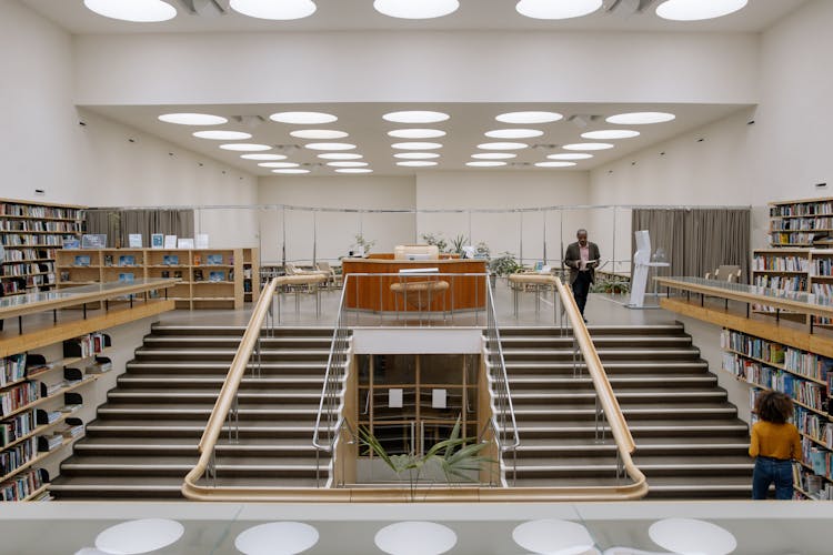 Black Man With Book Near Stairs In Public Library