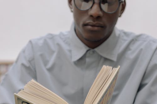 Man in White Dress Shirt Wearing Black Framed Eyeglasses Reading a Book