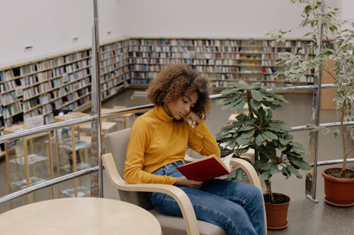 Woman in Yellow Long Sleeve Shirt and Blue Denim Jeans Sitting on White Chair