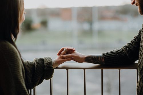 Free Side view of crop anonymous content hipster man and girlfriend holding hands on fenced balcony in daytime Stock Photo