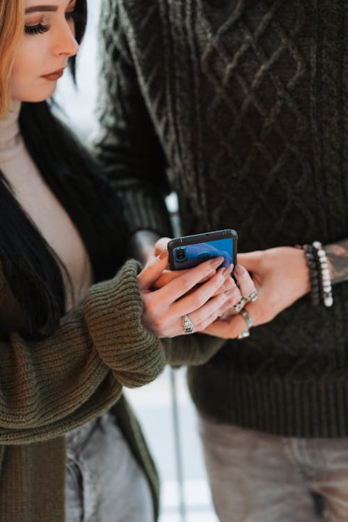 青いスマートフォンを保持している茶色のニットセーターの女性