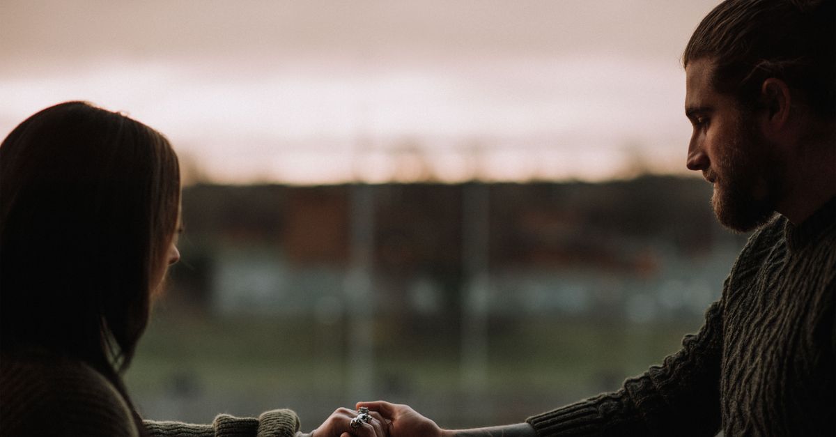 Side view of crop unshaven male holding hand of female beloved on balcony at sundown
