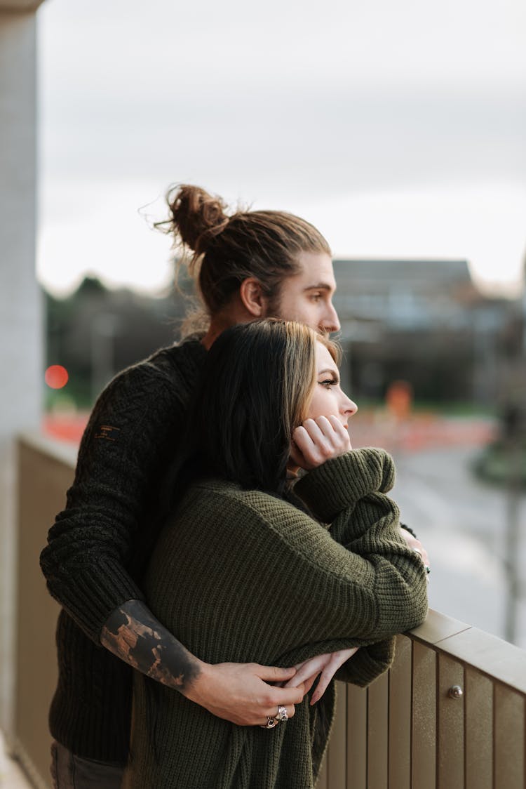 Couple Embracing And Contemplating City From Balcony