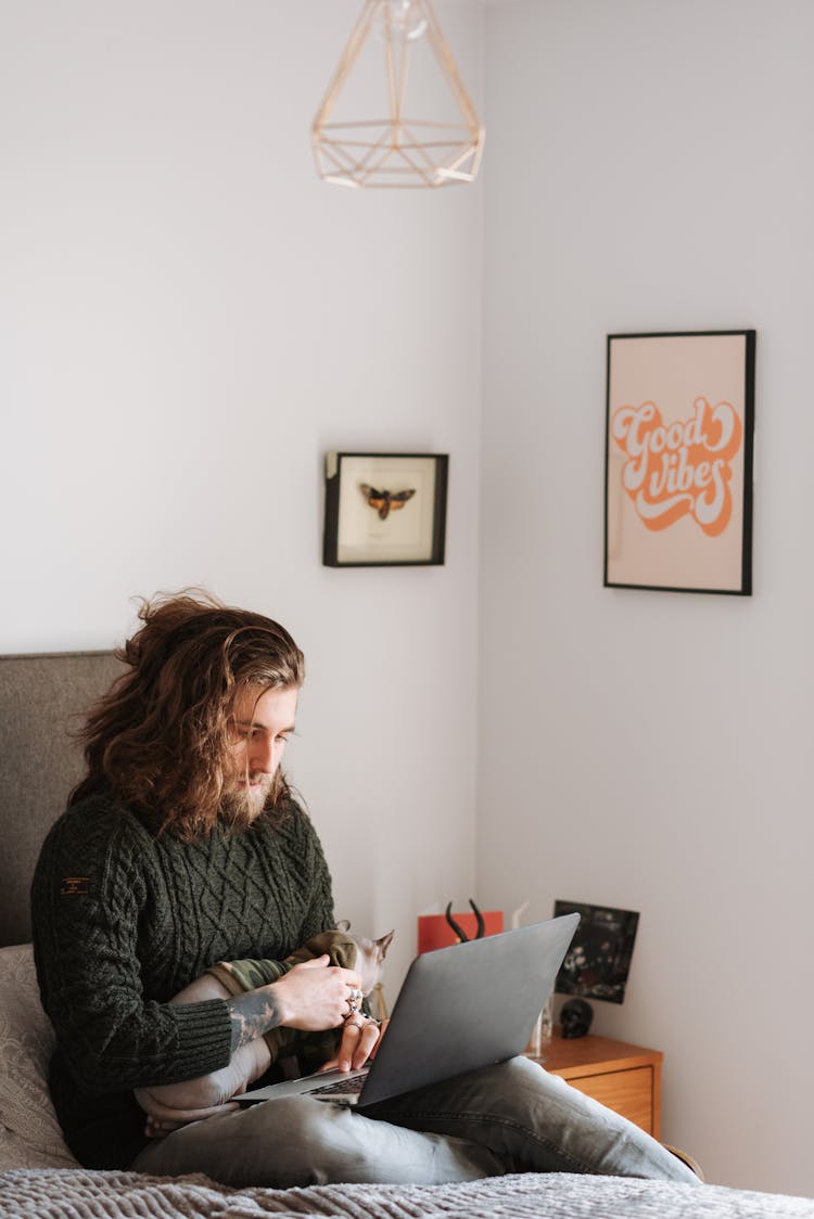 Hipster Man With Cat Surfing Internet On Laptop On Bed