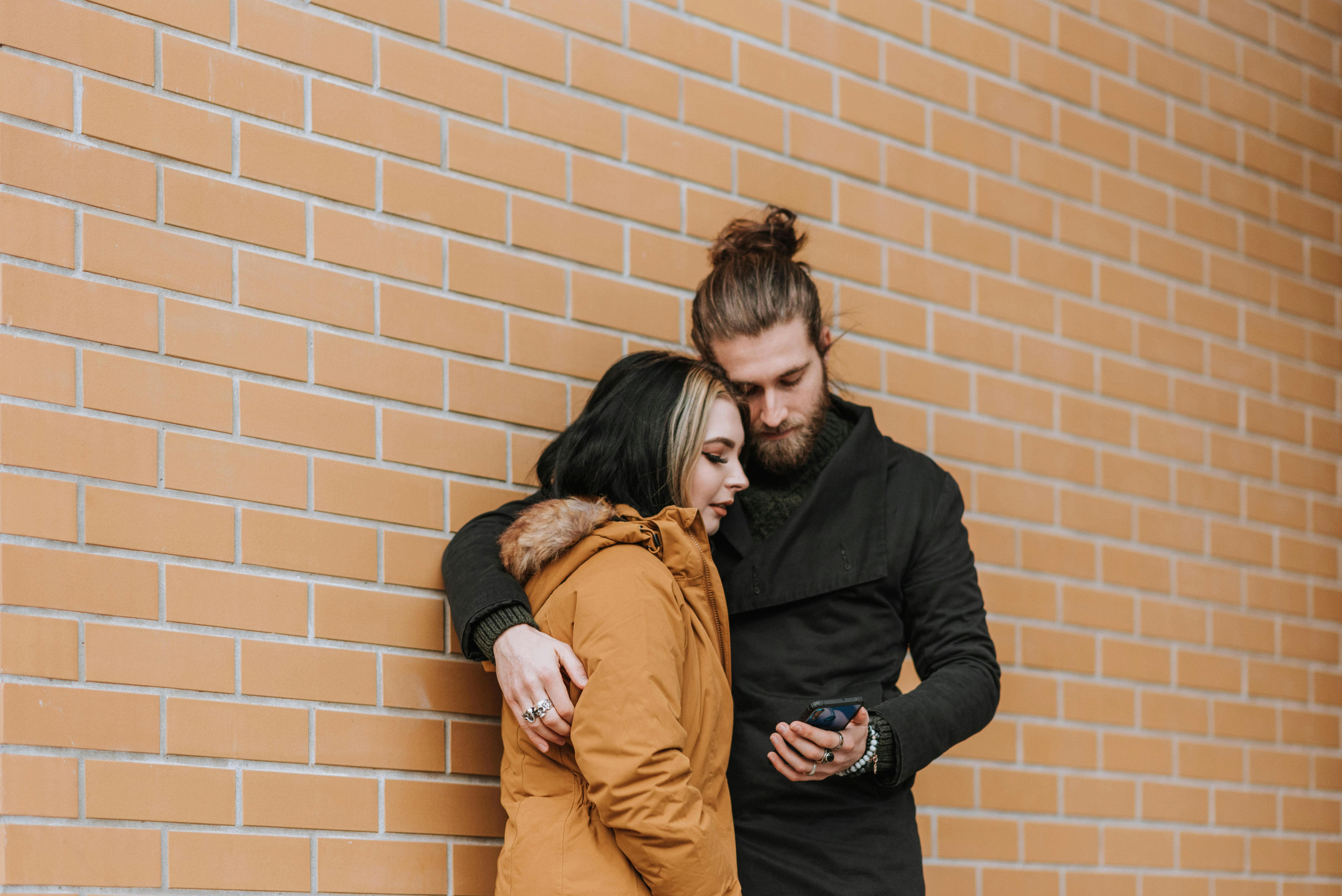 couple sharing smartphone near brick wall on street