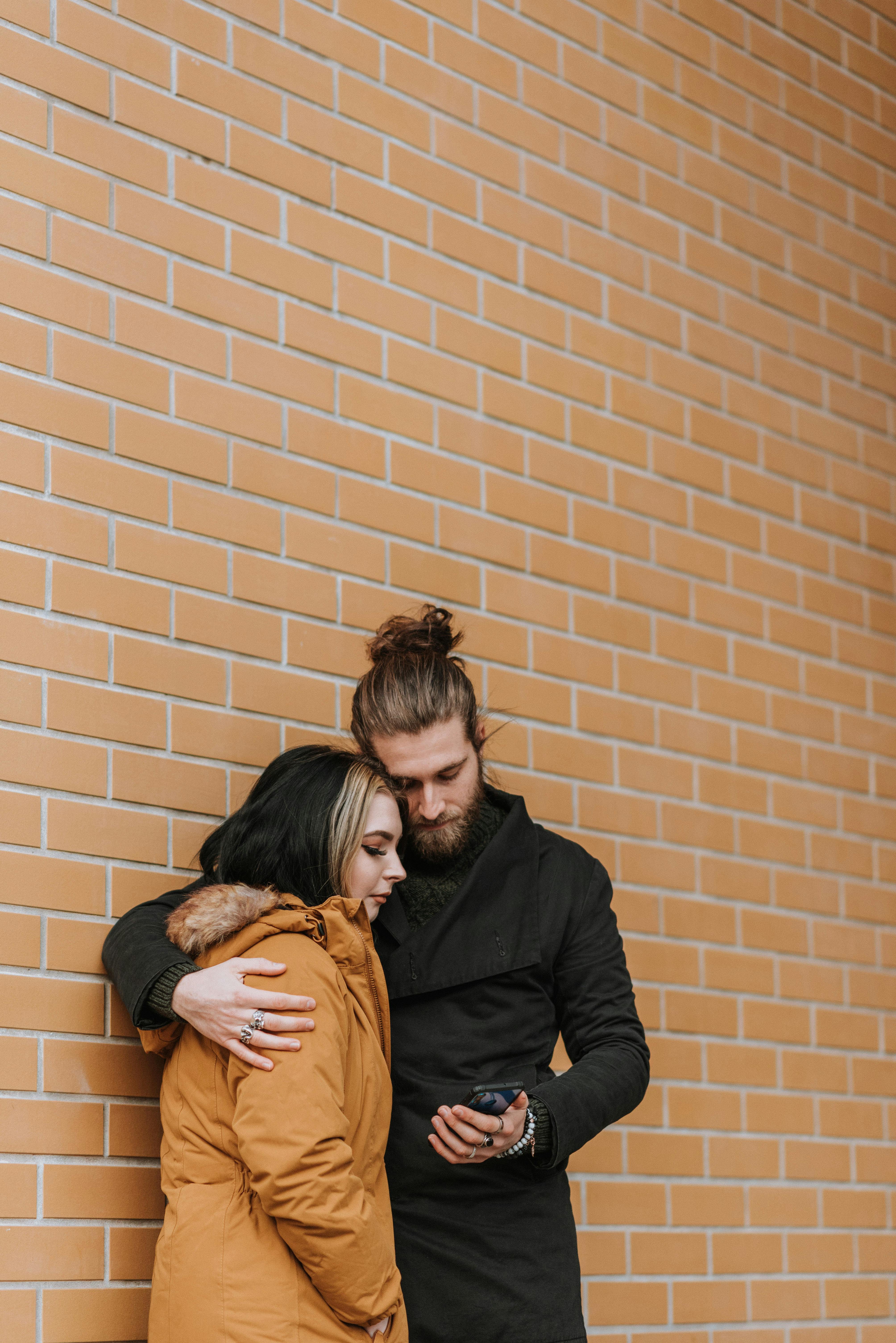 young couple embracing and sharing smartphone near brick building