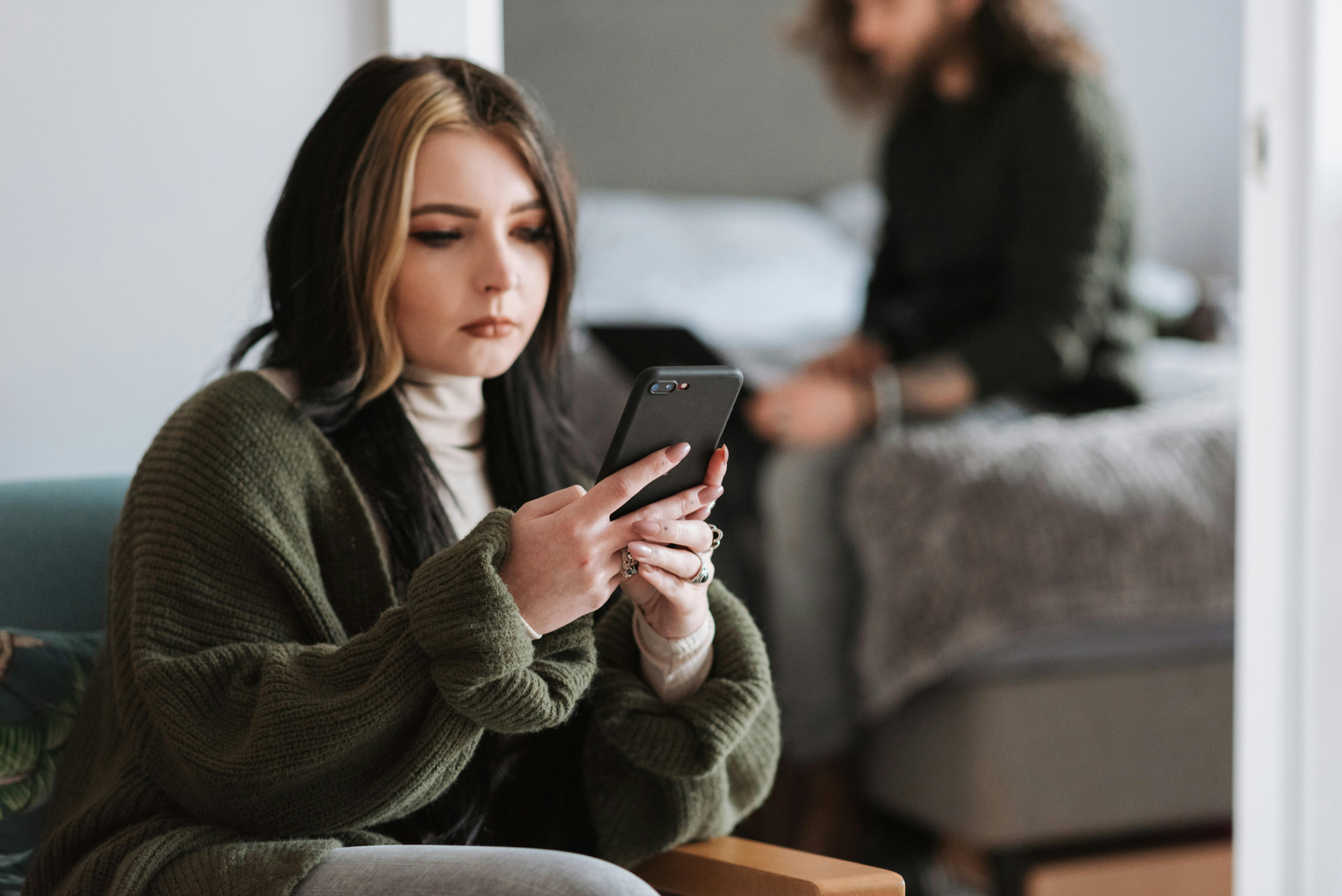 thoughtful young woman messaging on smartphone near boyfriend typing on netbook