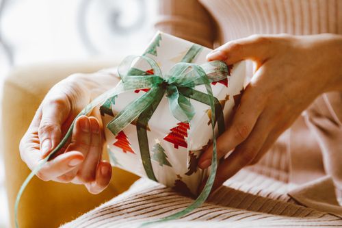 Free Close-up of hands holding a Christmas gift with tree design, wrapped in festive paper. Stock Photo