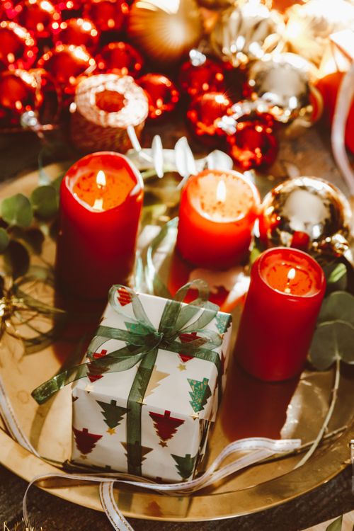 Free A cozy Christmas scene featuring lit candles, red baubles, and a wrapped gift on a metal tray. Stock Photo
