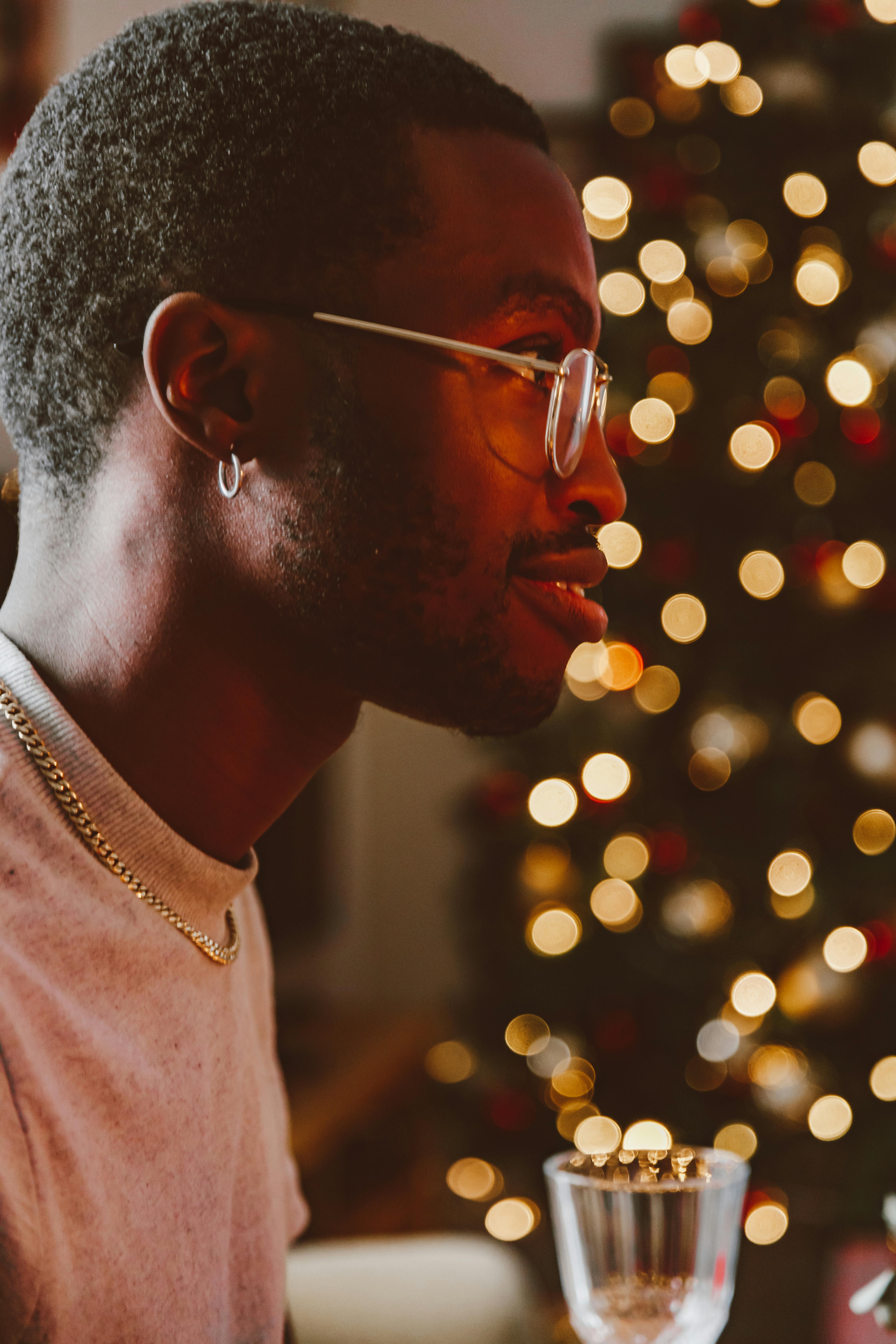A thoughtful profile of a man in a cozy festive setting, adorned with lights and a visible Christmas tree.