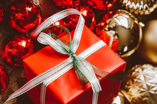 Free A beautifully wrapped Christmas gift surrounded by red and gold ornaments, perfect for holiday celebrations. Stock Photo