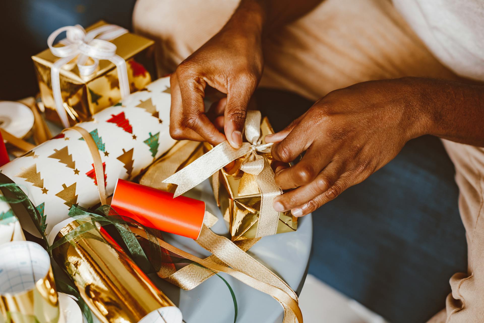 Hands tying ribbons on Christmas gifts with festive wrapping paper and gold accents.