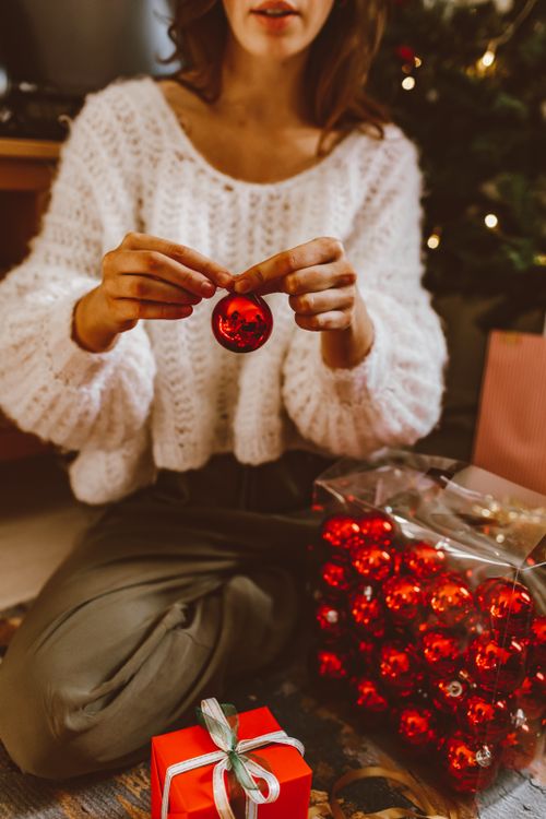 Free Woman decorating for Christmas with red baubles and a wrapped gift box. Stock Photo