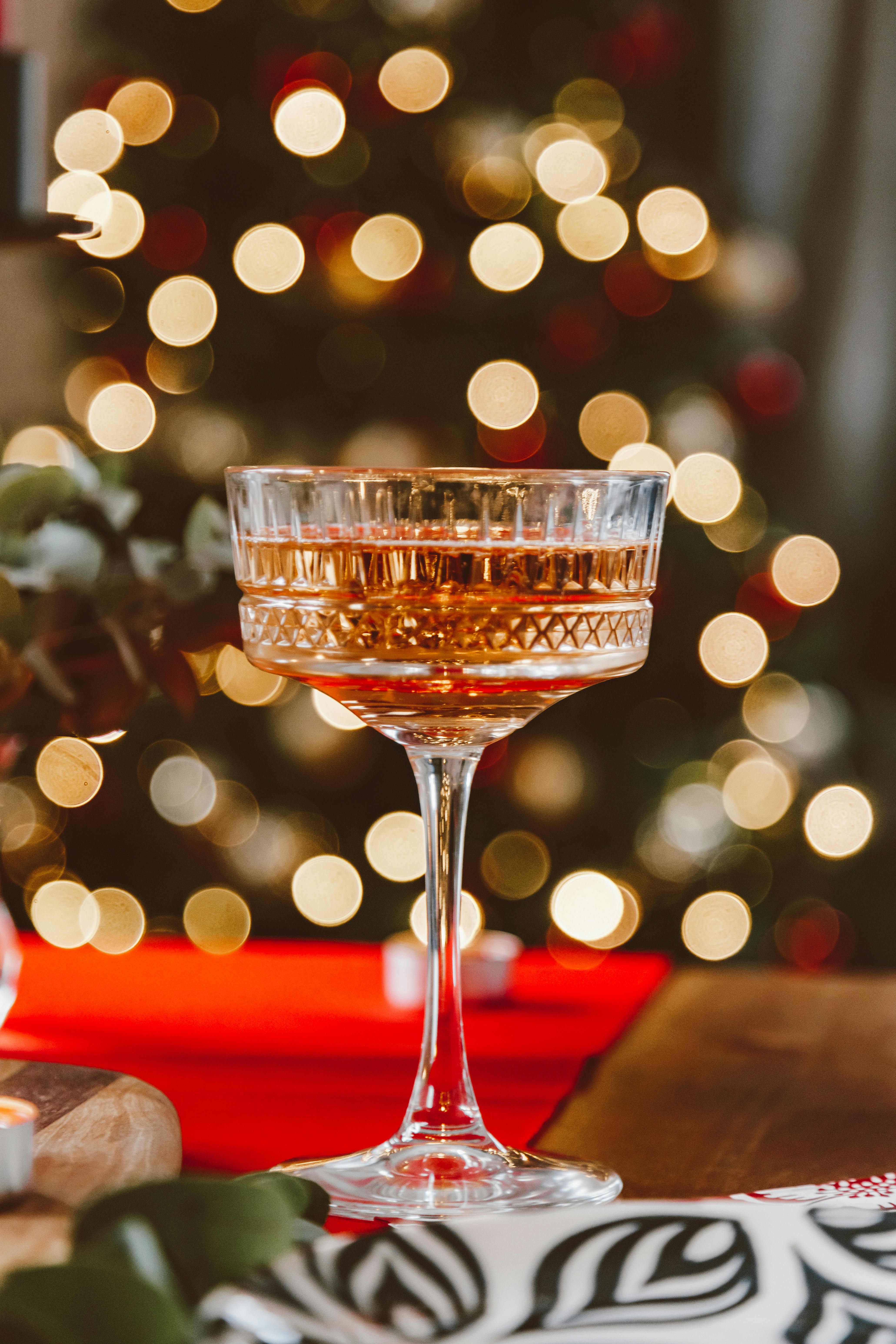 Elegant champagne glass with bokeh lights and Christmas tree background, evoking holiday celebration.