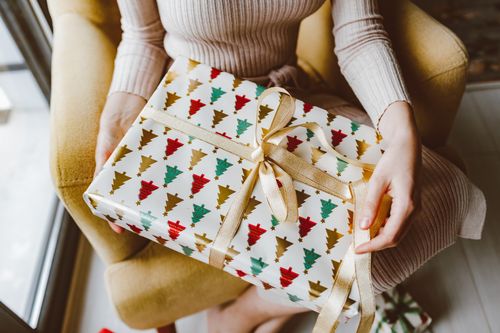 Free Woman holding beautifully wrapped Christmas gift with ribbon, creating a warm holiday ambiance. Stock Photo