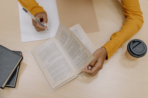 Человек в желтой рубашке с длинным рукавом с белой ручкой пишет на белой бумаге