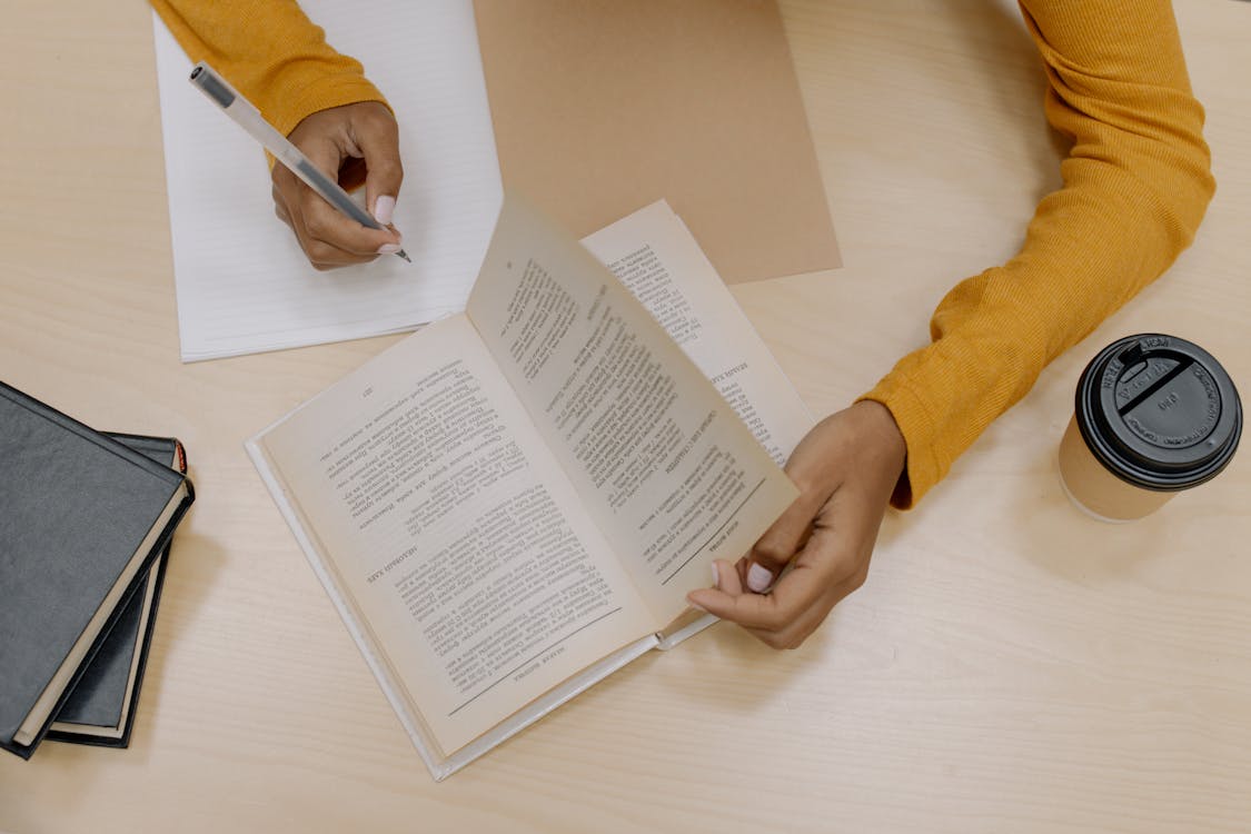 Person in Yellow Long Sleeve Shirt Holding White Pen Writing on White Paper