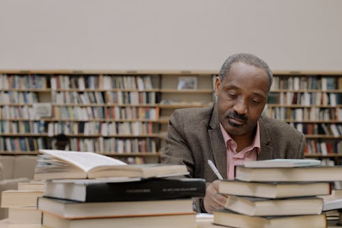 Man in Gray Suit Jacket Sitting Beside Books