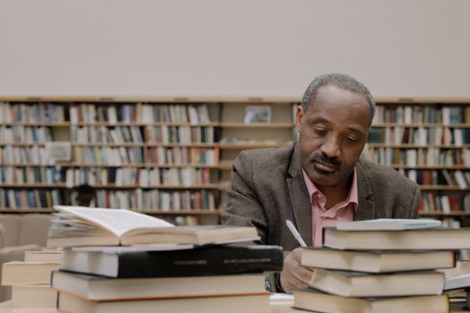 Man sits and studies with books in a library, emphasizing focus and learning.