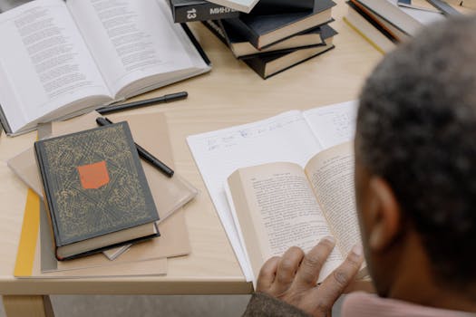 A person engaged in study with an array of books in a quiet library setting.
