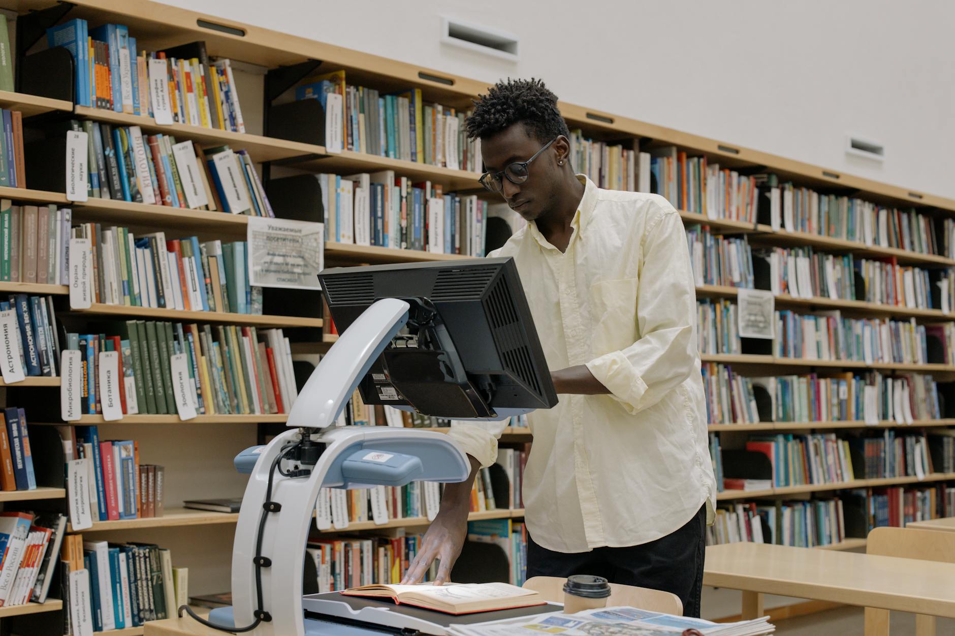 An African American man scanning books in a modern public library surrounded by bookshelves.