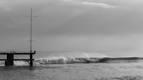 Grayscale Photo of Sea Waves Crashing on Wooden Dock