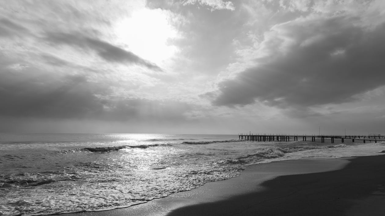 Grayscale Photo of Sunlight on a Cloudy Sky Above Sea · Free Stock Photo