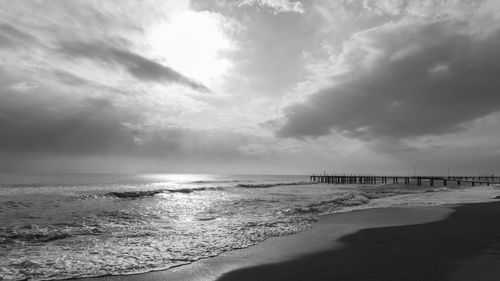Free Serene black and white beachscape featuring waves and a pier under dramatic cloudy skies. Stock Photo