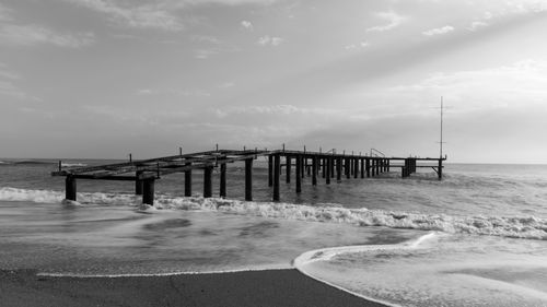 Free A serene monochrome view of an old pier extending into the ocean with gentle waves and overcast sky. Stock Photo
