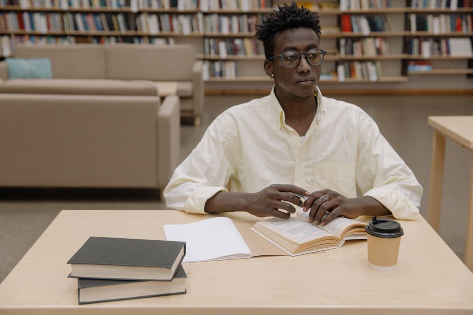 Young man intensely studying in a library setting, surrounded by books.