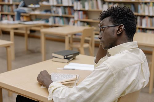 Free Young adult studying intently in a library with books and empty desks around. Stock Photo