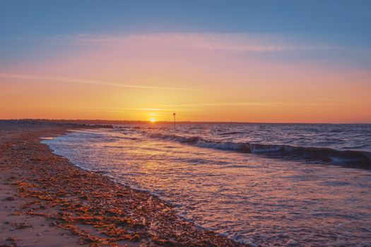 Captivating sunrise over a tranquil beach in England, showcasing vibrant colors and gentle waves.