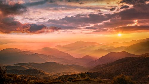 Free Beautiful sunset casting warm hues over a vast mountain landscape with dramatic clouds. Stock Photo