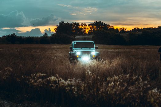 An off-road vehicle navigating through a grassy field during a vibrant sunset, showcasing adventure and nature.