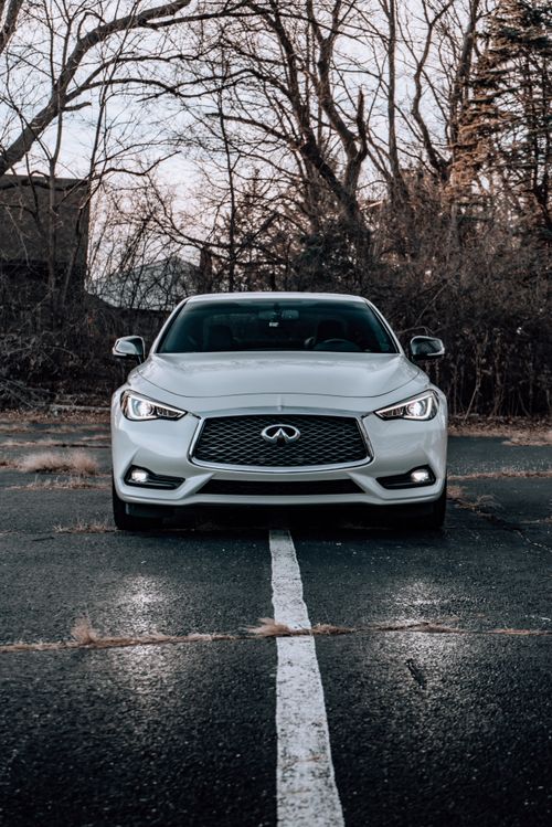 Free A modern white Infiniti sportscar parked on a wet asphalt road surrounded by trees. Stock Photo