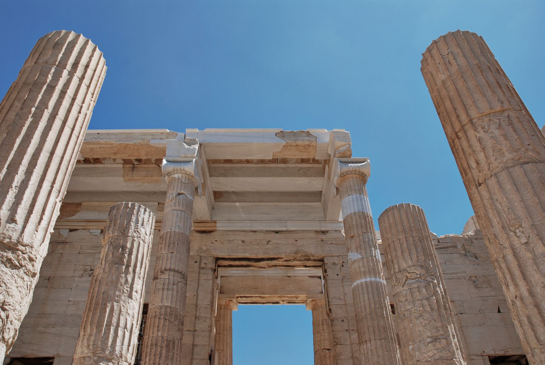 Low angle view of ancient Greek columns under a clear blue sky in Athens.