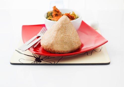 A traditional Nigerian dish elegantly presented on a vibrant red plate, accompanied by a colorful vegetable stew.