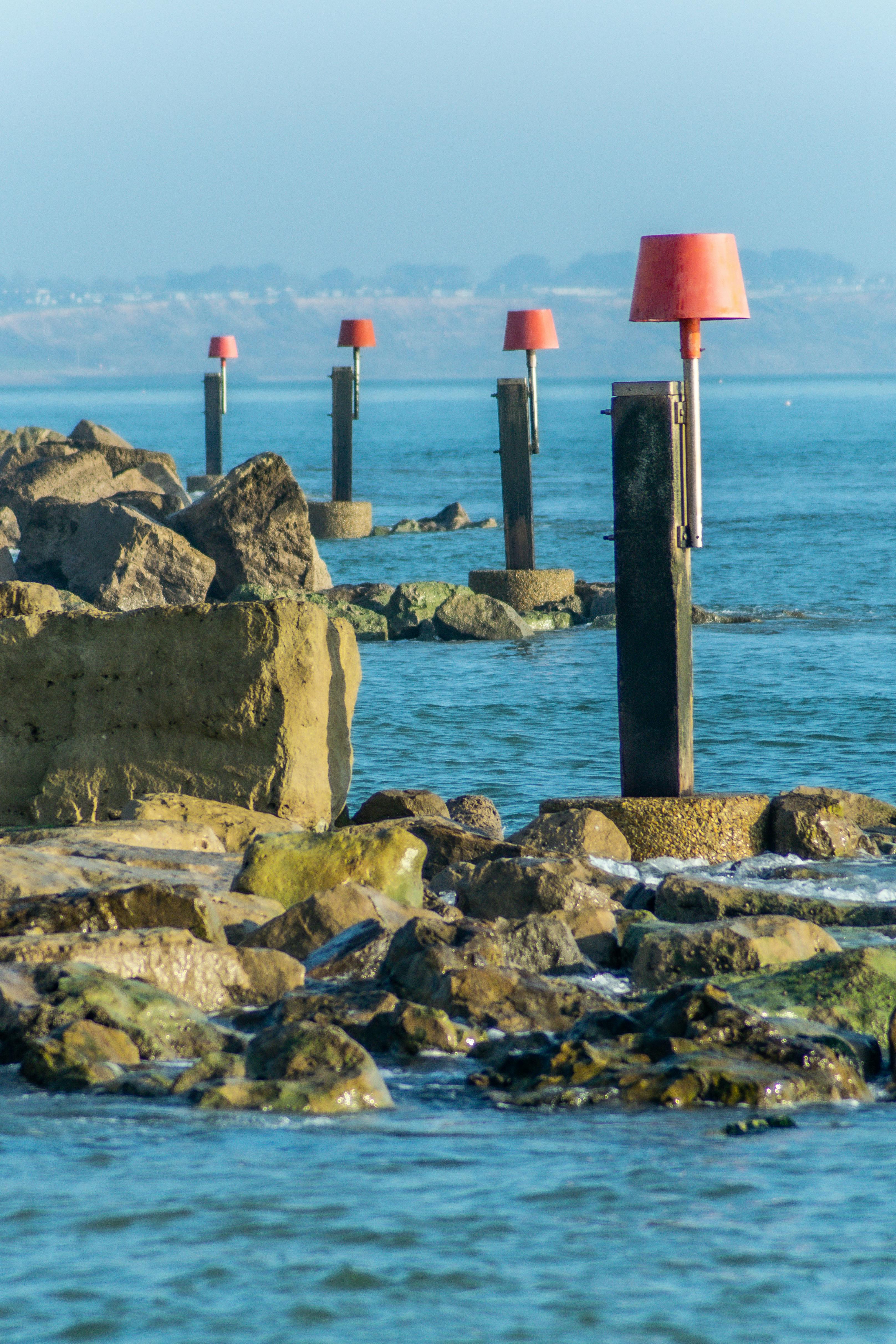 brown rocks on sea shore with red nautical warning beacons
