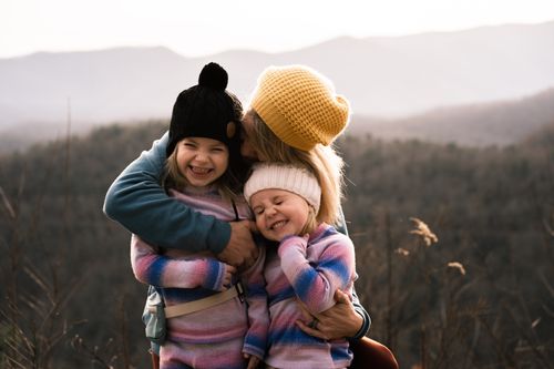 Free Mother embracing daughters with smiles in Asheville's scenic fall landscape. Stock Photo